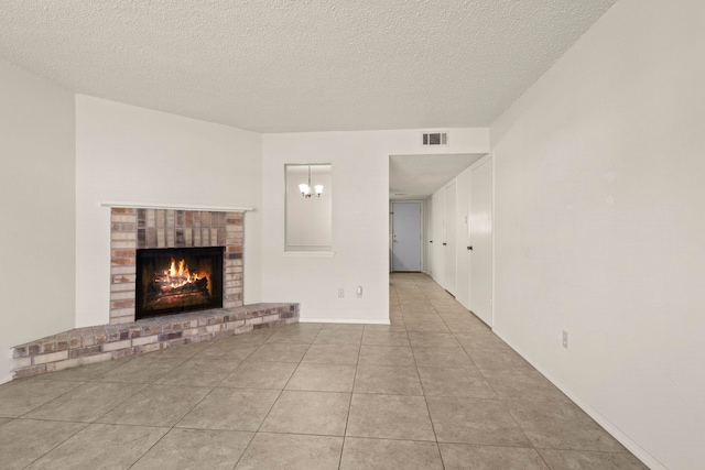 unfurnished living room featuring a textured ceiling, an inviting chandelier, a fireplace, tile patterned flooring, and visible vents