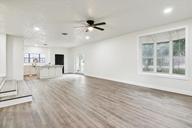 unfurnished living room with a textured ceiling, light hardwood / wood-style flooring, and ceiling fan