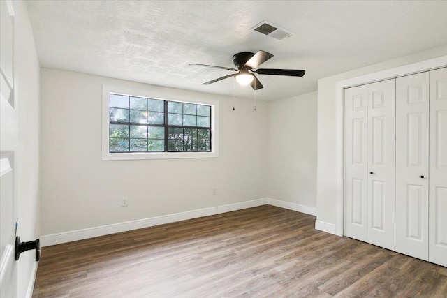 unfurnished bedroom with a textured ceiling, dark hardwood / wood-style flooring, a closet, and ceiling fan