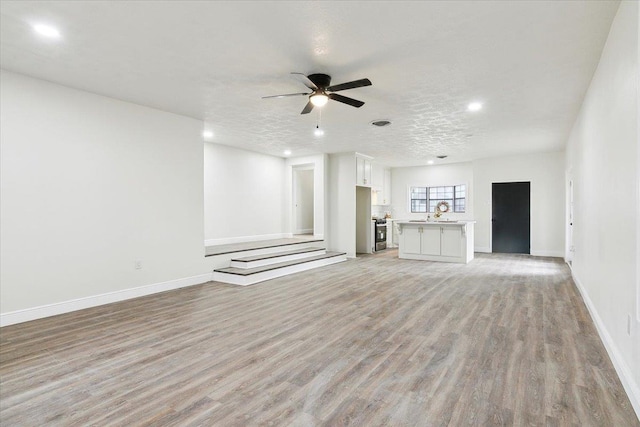 unfurnished living room featuring ceiling fan, a textured ceiling, and light wood-type flooring