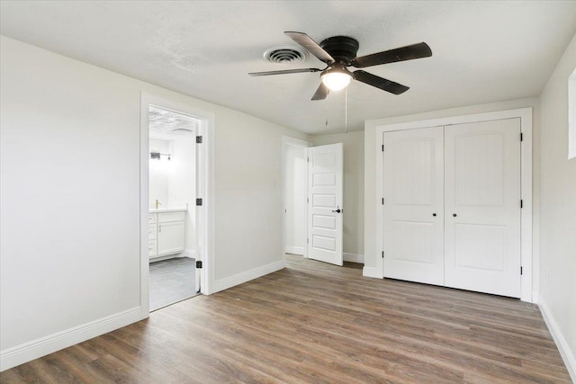 unfurnished bedroom featuring ceiling fan, dark hardwood / wood-style floors, connected bathroom, and a closet