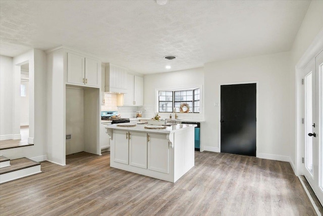 kitchen featuring a center island, premium range hood, white cabinets, light wood-type flooring, and stainless steel range