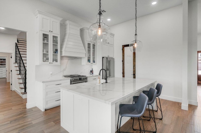 kitchen with hanging light fixtures, a kitchen island with sink, premium range hood, high quality appliances, and white cabinets