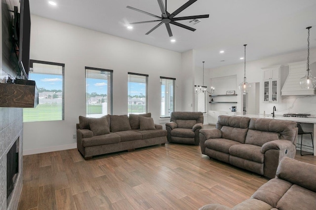 living room featuring ceiling fan with notable chandelier, a tile fireplace, and light hardwood / wood-style flooring