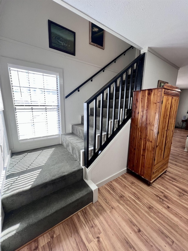 stairway with a textured ceiling and wood finished floors