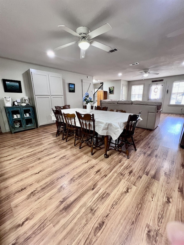 dining space with visible vents, light wood-style floors, a ceiling fan, a textured ceiling, and stairs