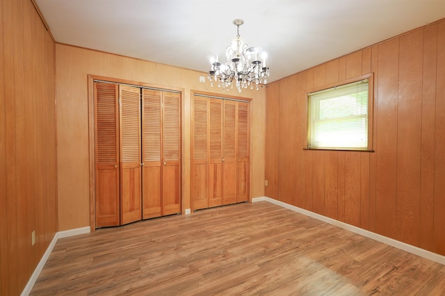 unfurnished bedroom with wood walls, two closets, wood-type flooring, and a chandelier