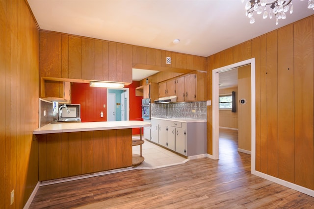 kitchen with sink, light hardwood / wood-style flooring, kitchen peninsula, oven, and decorative backsplash