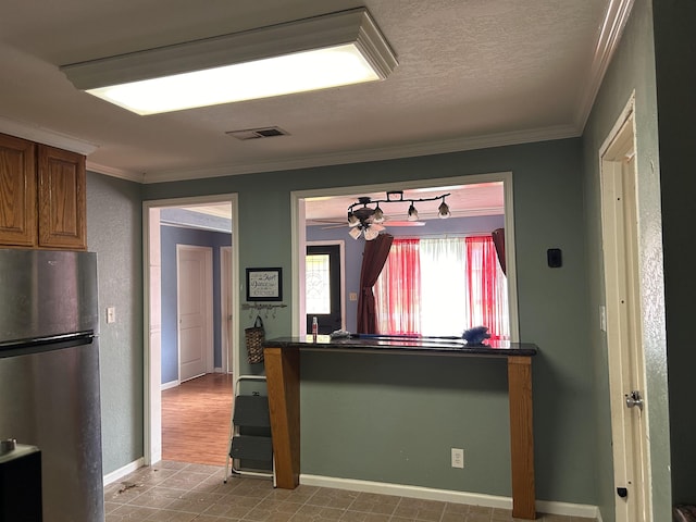 kitchen featuring a textured ceiling, ceiling fan, crown molding, and stainless steel refrigerator