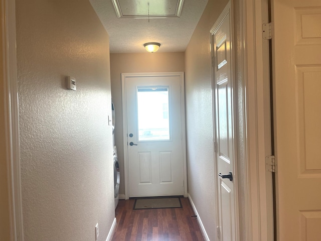doorway to outside with a textured ceiling, stacked washer and clothes dryer, and dark hardwood / wood-style floors