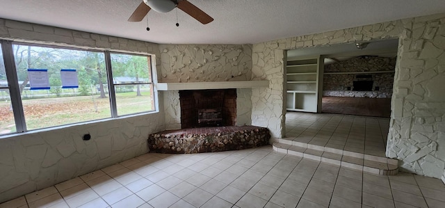 unfurnished living room with ceiling fan, a fireplace, light tile patterned floors, and a textured ceiling