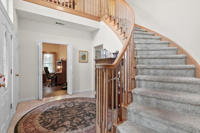 stairway with tile patterned floors and a towering ceiling