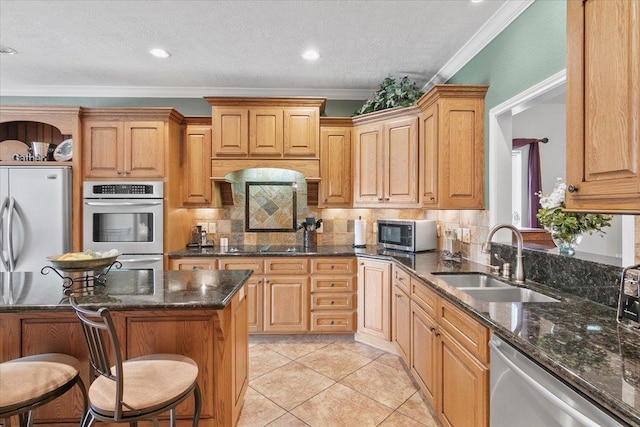 kitchen with a kitchen bar, dark stone counters, stainless steel appliances, crown molding, and sink