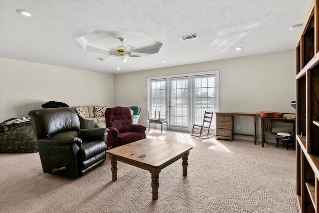 living room with a textured ceiling, light colored carpet, a raised ceiling, and ceiling fan