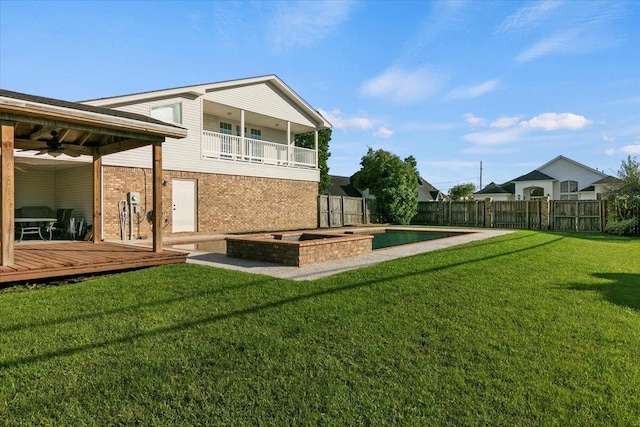 back of property featuring a jacuzzi, a yard, a balcony, and a wooden deck