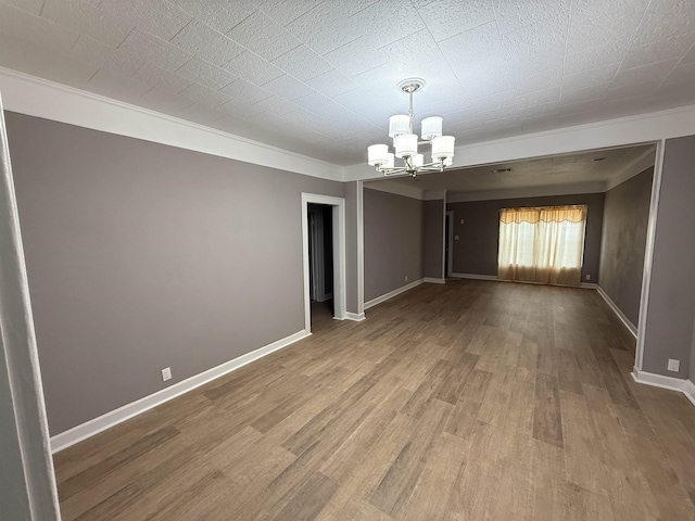 empty room with crown molding, baseboards, a chandelier, and wood finished floors