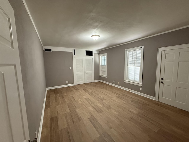 unfurnished bedroom featuring baseboards, ornamental molding, wood finished floors, and visible vents