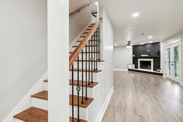 stairs featuring ceiling fan, a fireplace, and wood-type flooring