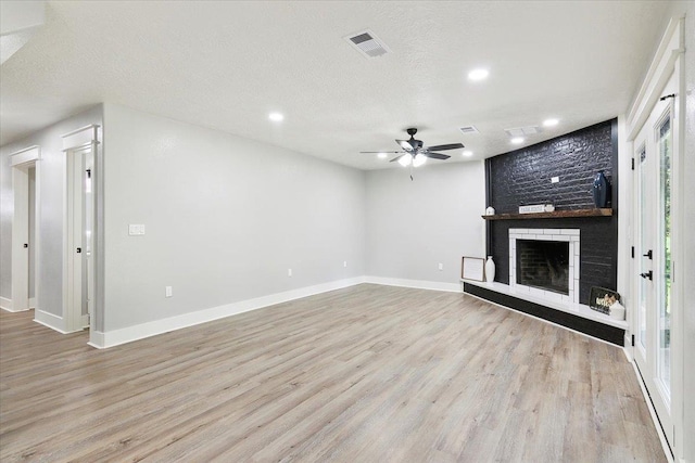 unfurnished living room with a textured ceiling, ceiling fan, light wood-type flooring, and a fireplace