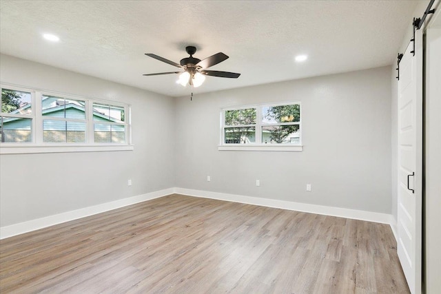 unfurnished bedroom with ceiling fan, a barn door, light hardwood / wood-style floors, and multiple windows