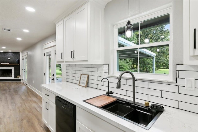 kitchen with light stone countertops, dishwasher, white cabinets, and sink