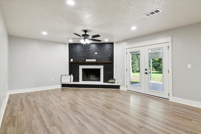 unfurnished living room featuring french doors, light wood-type flooring, a brick fireplace, a textured ceiling, and ceiling fan