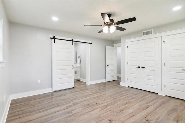 unfurnished bedroom with a barn door, ceiling fan, light hardwood / wood-style flooring, and ensuite bathroom