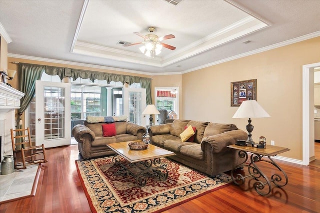 living room featuring a raised ceiling, hardwood / wood-style floors, visible vents, and a healthy amount of sunlight