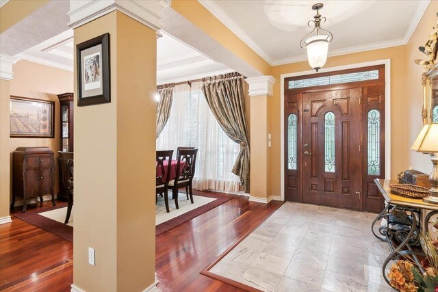 entryway featuring baseboards, ornamental molding, wood finished floors, and decorative columns