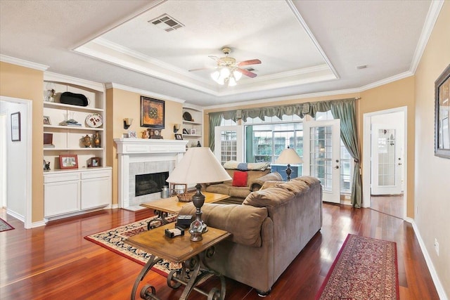living area with a tray ceiling, wood finished floors, a ceiling fan, crown molding, and a fireplace