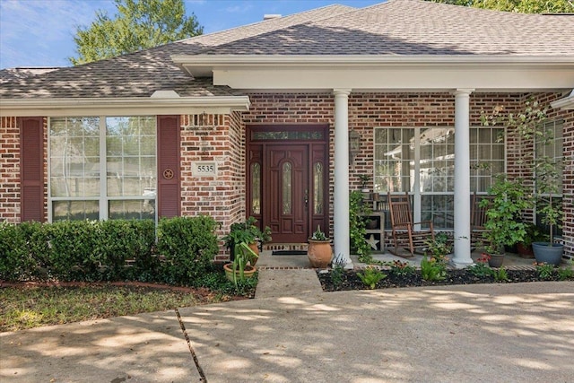 doorway to property with brick siding and a shingled roof