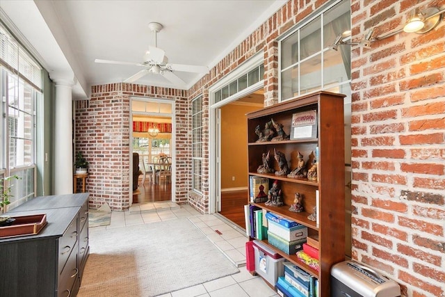 interior space with brick wall, a ceiling fan, and light tile patterned floors
