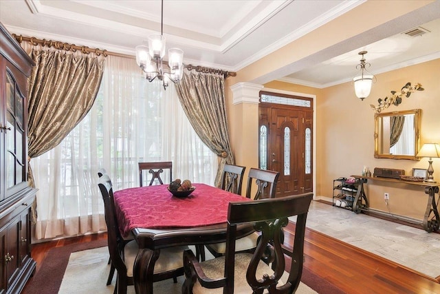 dining room with crown molding, wood finished floors, a tray ceiling, a notable chandelier, and visible vents