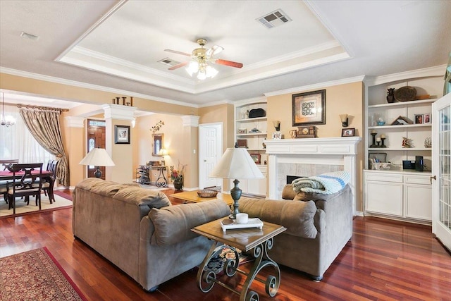 living area with dark wood-style flooring, visible vents, built in shelves, ceiling fan, and a raised ceiling