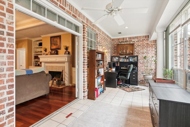 tiled home office featuring brick wall, ornamental molding, ceiling fan, and a healthy amount of sunlight
