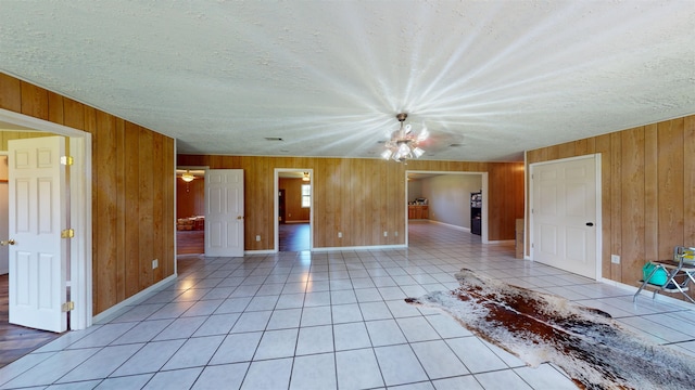 tiled empty room featuring an inviting chandelier, a textured ceiling, and wood walls