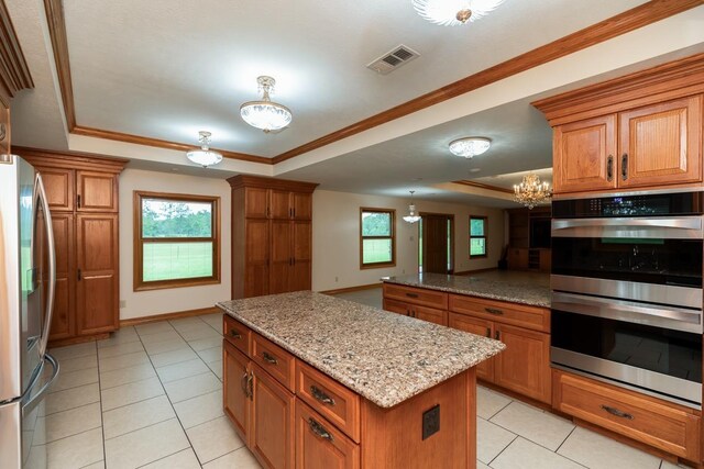 114 Holmes Rd, Lumberton, TX 77657 - kitchen featuring a tray ceiling, appliances with stainless steel finishes, brown cabinetry, light tile patterned floors, and a kitchen island
