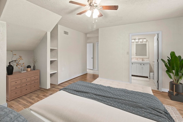 bedroom featuring visible vents, a sink, light wood-style floors, a textured ceiling, and connected bathroom