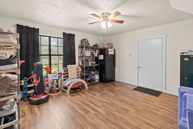 recreation room with baseboards, a textured ceiling, ceiling fan, and wood finished floors