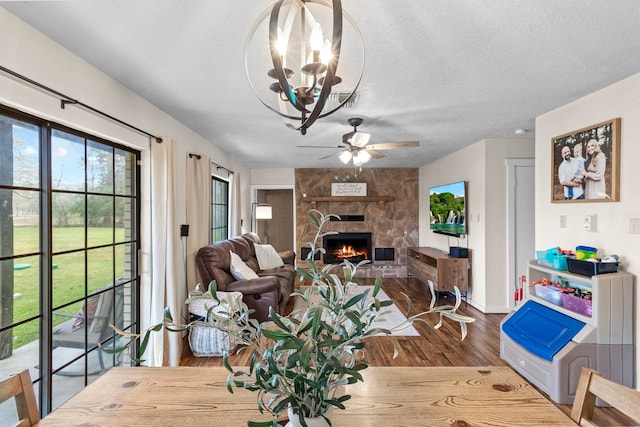 dining room with a textured ceiling, a stone fireplace, wood finished floors, and a ceiling fan