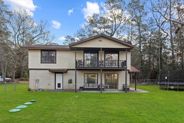 back of house with a patio, a trampoline, a lawn, and brick siding