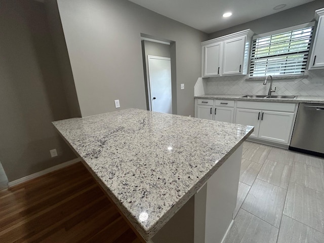 kitchen with white cabinets, stainless steel dishwasher, light stone countertops, and sink