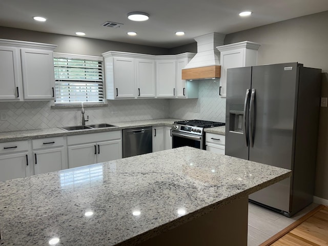 kitchen featuring light stone countertops, sink, white cabinets, custom range hood, and appliances with stainless steel finishes