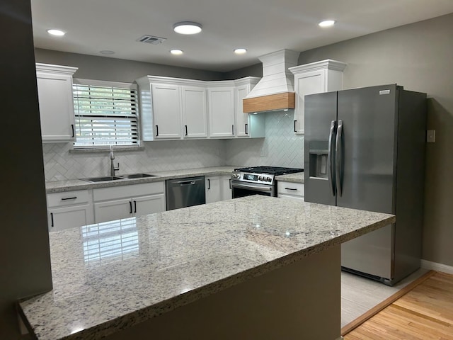 kitchen featuring light stone counters, custom range hood, stainless steel appliances, sink, and white cabinetry