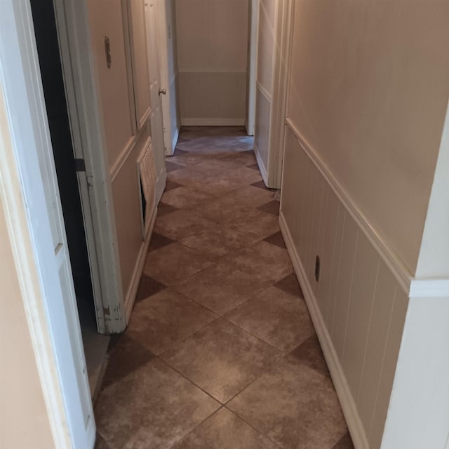 hallway with tile patterned floors, a decorative wall, and wainscoting