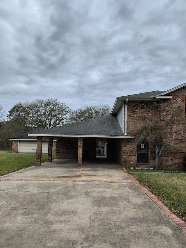 exterior space with driveway, a yard, an attached garage, a shingled roof, and brick siding