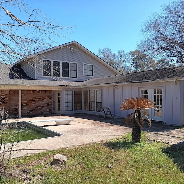 back of property with brick siding, board and batten siding, and a patio