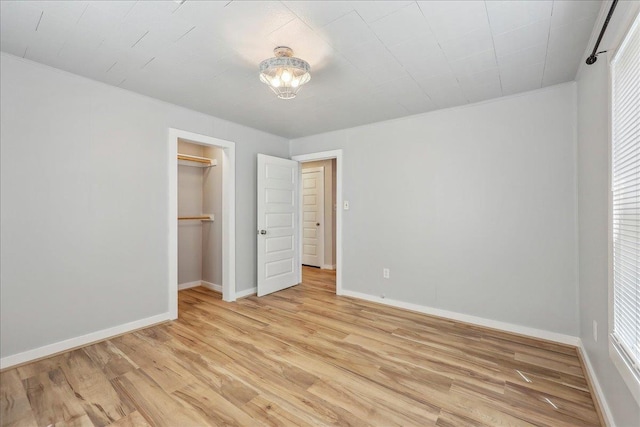 unfurnished bedroom with light wood finished floors, baseboards, a closet, and a walk in closet