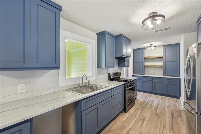 kitchen featuring gas range oven, freestanding refrigerator, a sink, open shelves, and a textured ceiling