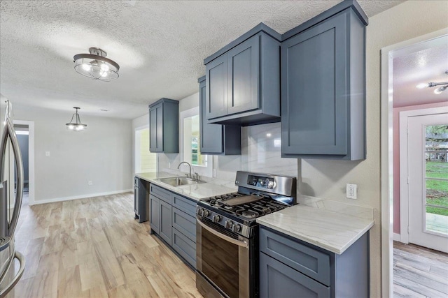 kitchen featuring appliances with stainless steel finishes, a sink, light wood-style flooring, healthy amount of natural light, and a textured ceiling